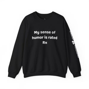 May include: Black crew neck sweatshirt with the text "My sense of humor is rated Rx" in white. The right sleeve has the text "Pharmacist Pillosophy" in white. A casual, comfortable top.
