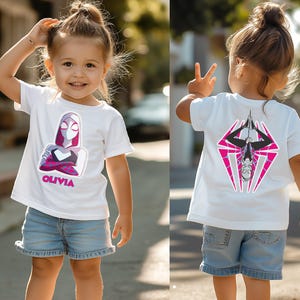 Puede incluir: Camiseta blanca con un gr&aacute;fico de superh&eacute;roe en la parte delantera y trasera. El dise&ntilde;o frontal incluye una ilustraci&oacute;n de personaje y el nombre "OLIVIA" en rosa. La parte trasera muestra un emblema de superh&eacute;roe a juego en rosa y negro.