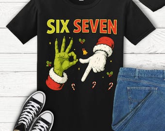 May include: Black t-shirt with the text "SIX SEVEN" in yellow and red. The graphic features a green hand making an "OK" sign and a white hand pointing, both with Santa-style cuffs. Candy canes and holly accents complete the design.