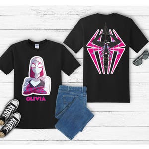 Puede incluir: Camisetas negras con dise&ntilde;os gr&aacute;ficos. Una camiseta presenta un personaje con una m&aacute;scara blanca y rosa y el nombre "OLIVIA". La otra camiseta muestra un dise&ntilde;o de telara&ntilde;a rosa y blanca. Incluye vaqueros azules y zapatillas negras.