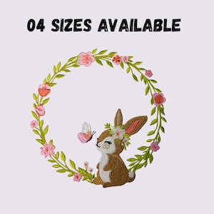 Puede incluir: Diseño bordado con un conejito marrón con una corona floral, una mariposa y una corona de flores rosas y hojas verdes. El texto "04 SIZES AVAILABLE" está en la parte superior. El diseño está sobre un fondo lila claro.