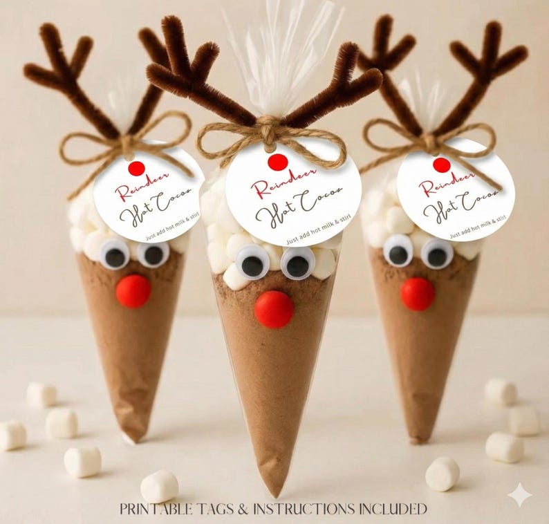May include: Three festive hot chocolate cones, each resembling a reindeer. They feature brown paper cones filled with cocoa, topped with marshmallows, googly eyes, and pipe cleaner antlers. Each has a tag that reads "Reindeer Hot Cocoa".