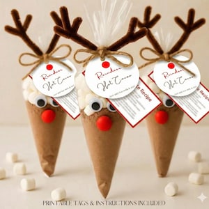 May include: Three festive reindeer hot chocolate cones. Each cone features a brown base, a red nose, googly eyes, and brown pipe cleaner antlers. White marshmallows sit atop the cocoa mix. Each cone has a tag that reads "Reindeer Hot Cocoa".