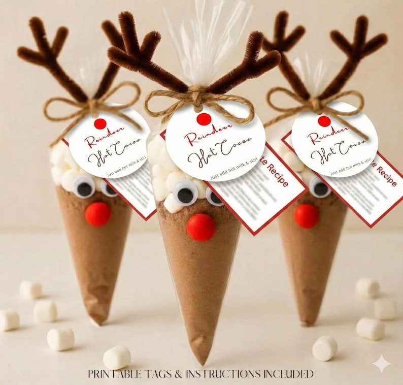 May include: Three festive reindeer hot chocolate cones. Each cone features a brown base, a red nose, googly eyes, and brown pipe cleaner antlers. White marshmallows sit atop the cocoa mix. Each cone has a tag that reads "Reindeer Hot Cocoa".