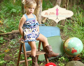 Puede incluir: Una niña pequeña con un vestido estampado en azul y blanco con volantes está sentada en un taburete de madera. Lleva botas de vaquero y tiene un lazo rosa en el pelo. El fondo incluye una maleta azul, un globo terráqueo y una muñeca de trapo roja.