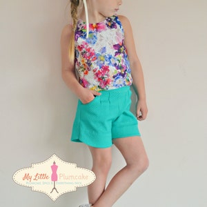 May include: A young girl wearing a floral print sleeveless top, teal shorts, and white shoes with gold accents. She is wearing a flower crown and has her hair in a braid. The image includes the text "My Little Plumcake Plumcake Spice & Everything Nice."