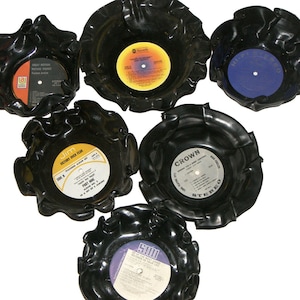 May include: Five black vinyl record coasters with different album covers. The coasters are shaped like a flower with ruffled edges. The album covers include "Great Motion Picture Themes", "Jim Victory Over Fear", "Crown", "High Fidelity", and "5001 Greatest Hits of Your Life".