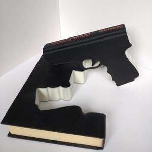 May include: A black book with the title "Double Cross" by Patterson on the spine. The book is shaped like a gun.
