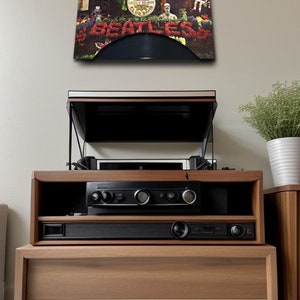 May include: A wooden entertainment center with a record player and audio components. The album cover of The Beatles' Sgt. Pepper's Lonely Hearts Club Band is displayed above. The cabinet has a natural wood finish and a modern design.