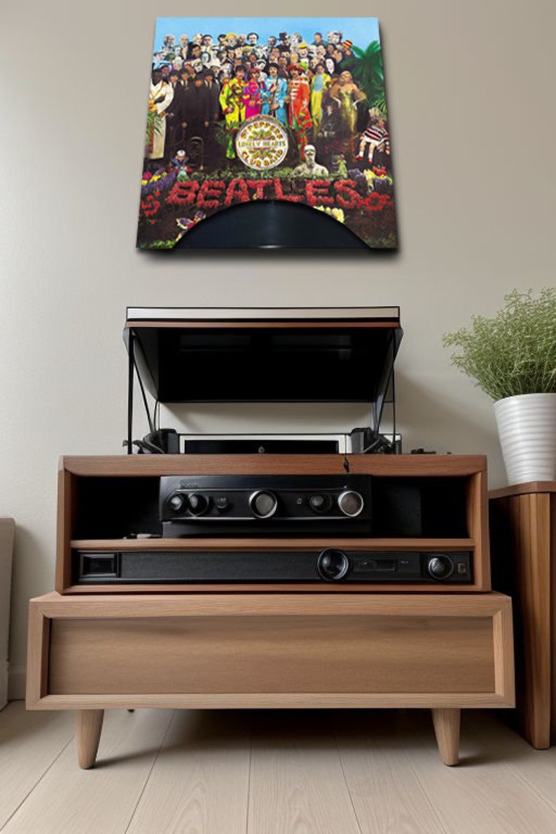 May include: A wooden entertainment center with a record player and audio components. The album cover of The Beatles' Sgt. Pepper's Lonely Hearts Club Band is displayed above. The cabinet has a natural wood finish and a modern design.