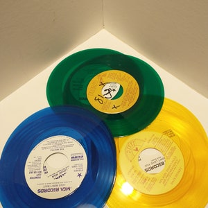 Small, shiny, round 45 size, vinyl records are displayed. The color of the album is blue, green, and yellow.