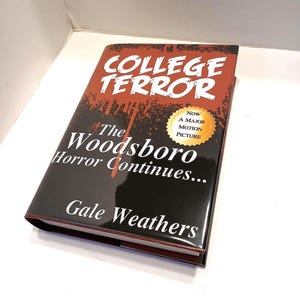 May include: A black and red book cover with the title "College Terror" in red letters. The subtitle is "The Woodsboro Horror Continues..." in white letters. The author's name, "Gale Weathers", is in white letters at the bottom of the cover. A gold sticker with the text "Now a Major Motion Picture" is on the cover.