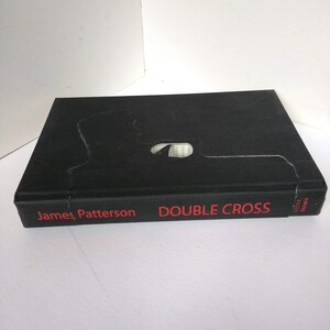 May include: A black hardcover book with the title "DOUBLE CROSS" in red text and the author "James Patterson" in red text. The book is published by Little, Brown.