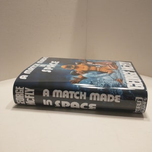 May include: A blue hardback book titled "A Match Made in Space" by George McFly. The cover features a colourful illustration of two astronauts in space.