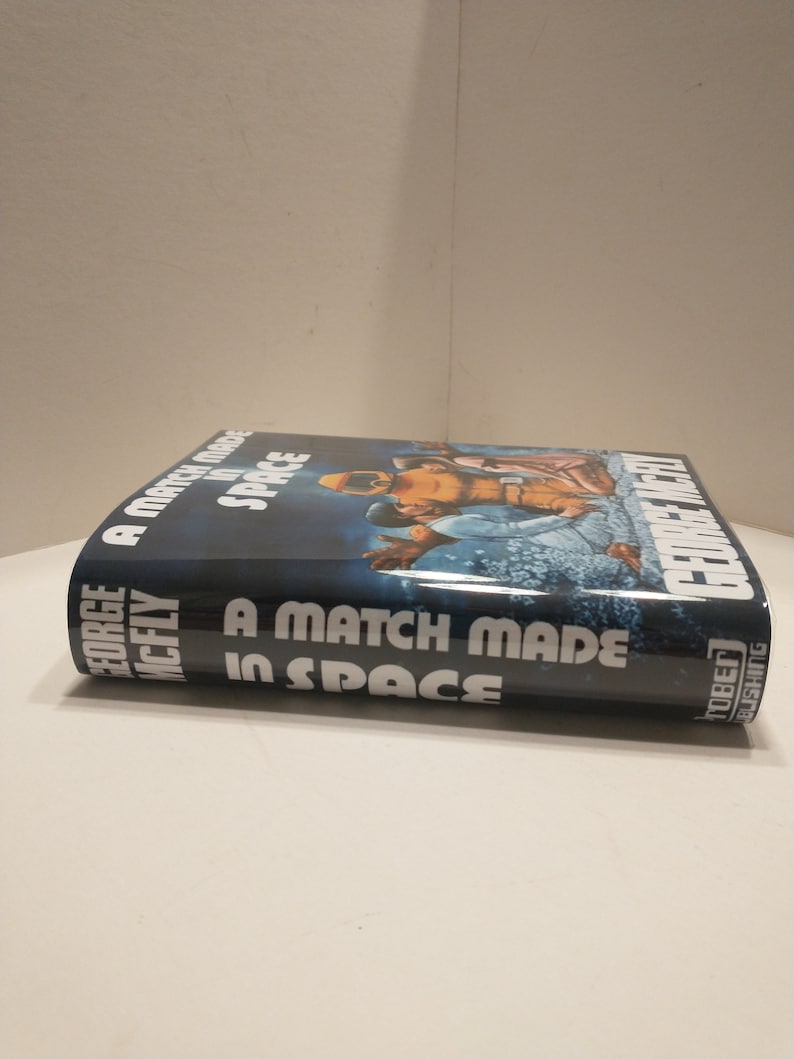 May include: A blue hardback book titled "A Match Made in Space" by George McFly. The cover features a colourful illustration of two astronauts in space.