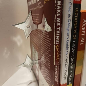 May include: A stack of books with a silver bookend shaped like a star. The books are titled "Don't Make Me Think! Revisited", "The Graphic Designer's Guide to Portfolio Design", "Dictionary of Graphic Design & Design", and "Pocket Pal".