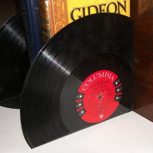 Shiny, round vinyl records cut on the back and bent on the bottom to make a bookend that holds up some books. The color of the album label is bright red.