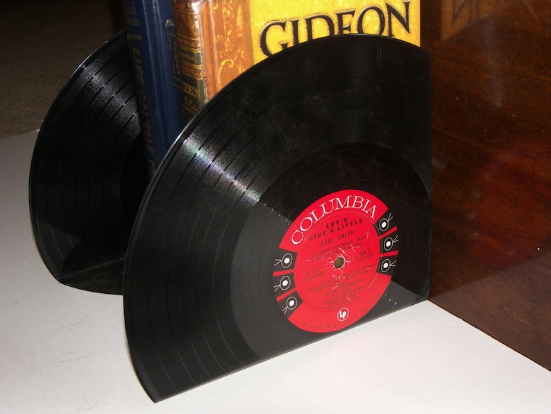 Shiny, round vinyl records cut on the back and bent on the bottom to make a bookend that holds up some books. The color of the album label is bright red.