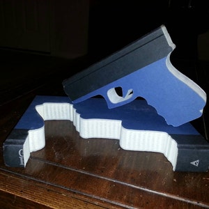 May include: A blue and black book with a gun-shaped cutout on the cover. The gun is made of paper and is blue with a black barrel.