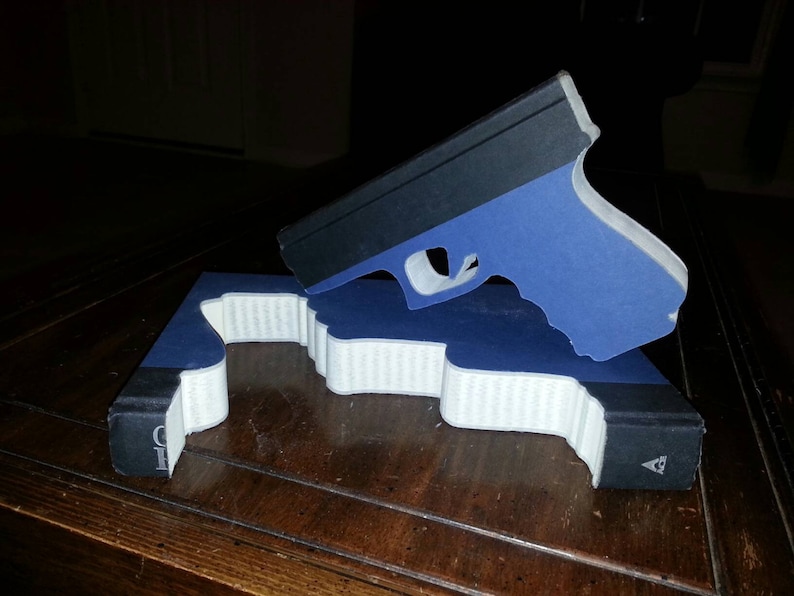 May include: A blue and black book with a gun-shaped cutout on the cover. The gun is made of paper and is blue with a black barrel.