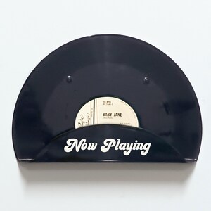 May include: Black vinyl record holder with the words "Now Playing" in white script. The holder displays a 45 RPM record with the label "Baby Jane". A stylish way to showcase your favorite vinyl.