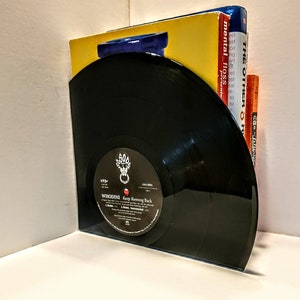 May include: A black vinyl record bookend with the text "WHODINI Keep Running Back" and a record label. The bookend holds several books with yellow, blue, and orange covers, creating a unique storage solution.