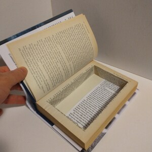 May include: A book with a hidden compartment inside the pages. The compartment is open and reveals a small space inside the book.
