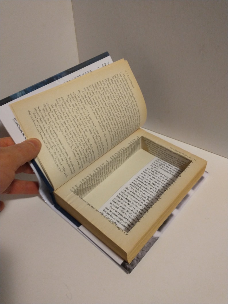 May include: A book with a hidden compartment inside the pages. The compartment is open and reveals a small space inside the book.