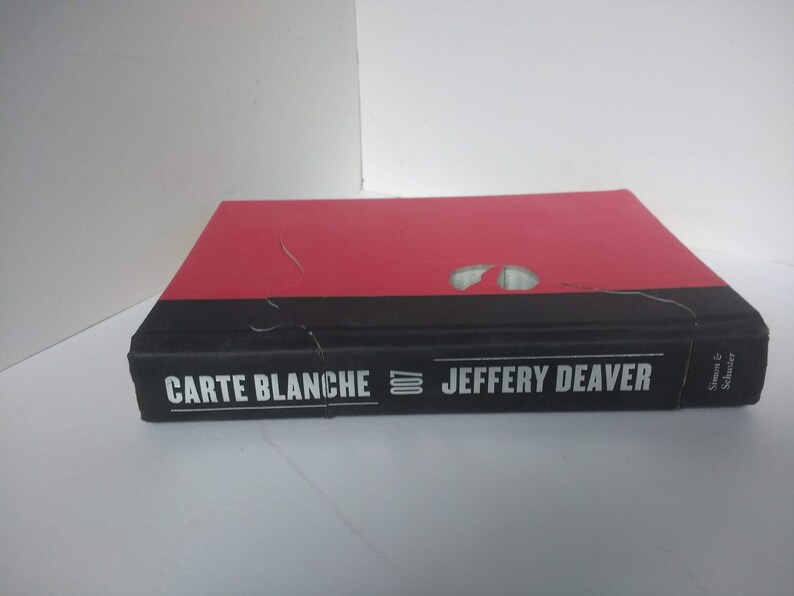 May include: A red and black hardcover book titled "Carte Blanche" by Jeffery Deaver, published by Simon & Schuster.