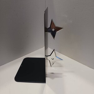 May include: A black metal bookend with two silver throwing stars attached to the side. The bookend is standing on a white surface.