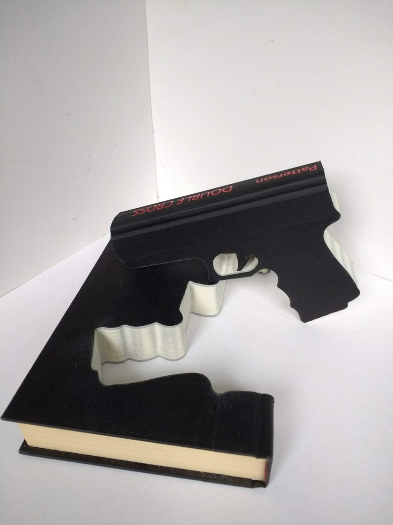 May include: A black book with the title "Double Cross" by Patterson on the spine. The book is shaped like a gun.