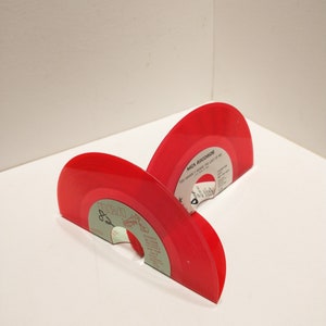 Small, shiny, round 45 size, vinyl records are bent on the bottom to make bookends. The color of the album is red.