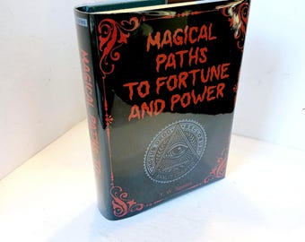 May include: A black book with a red title that reads "Magical Paths to Fortune and Power". The book has a red and black design with an all-seeing eye symbol on the front cover.
