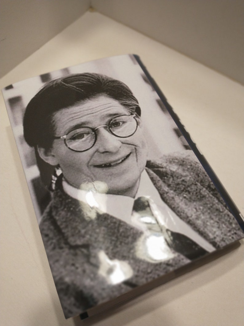 May include: Black and white photograph of a person wearing glasses and a suit jacket. The person is smiling and looking at the camera.