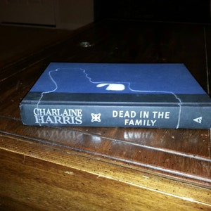 May include: A paperback book with a blue cover and white text. The title is "Dead in the Family" by Charlaine Harris.