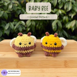 May include: Two small, round, crocheted bee plushies with yellow and brown striped bodies, white wings, and black bead eyes. The text BABY BEE ~ Crochet Pattern ~ is displayed above, and a PDF PATTERN ONLY label is at the bottom left.