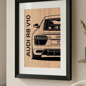 Può includere: Una stampa artistica da parete incorniciata che presenta un disegno a linee nere del retro di un'auto Audi R8 V10 su uno sfondo con venature del legno chiaro. Il testo AUDI R8 V10 è stampato verticalmente in nero sul lato sinistro.