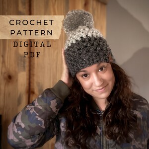 May include: A crochet hat pattern in digital PDF format. The hat is gray and white with a pom pom on top. The pattern is available for download.