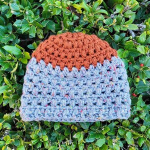 May include: A crocheted beanie hat with a brown top and a blue speckled bottom.