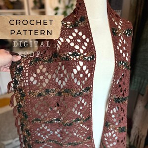 Pode incluir: Um xale de crochê marrom com detalhes vazados e franjas decorativas. O texto "CROCHET PATTERN DIGITAL PDF" é visível. O xale é exibido em um manequim, mostrando seu design e textura.