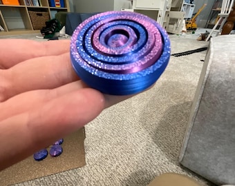 Peut inclure: Un ensemble de cinq anneaux empilables bleus et violets. Les anneaux sont faits d'un matériau lisse et brillant et ont une surface légèrement texturée. Les anneaux sont empilés en spirale, le plus grand anneau en bas et le plus petit en haut.