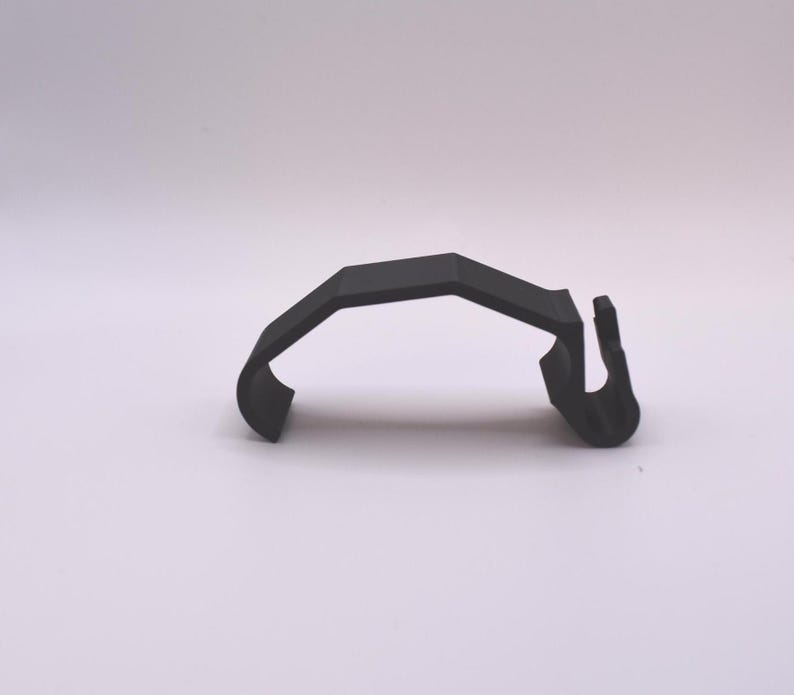 May include: A black plastic clip with a curved shape and a hook on one end.