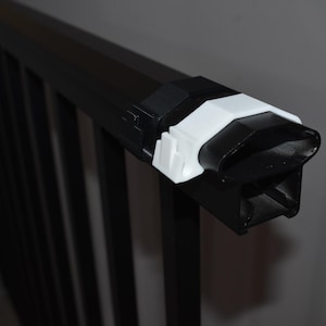 May include: Close-up of a black metal railing with white plastic end caps. The railing is designed for outdoor use and features a simple, modern design.
