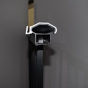 May include: Close-up of a black metal railing with a silver top. The top of the railing is designed with a series of grooves.