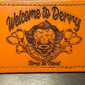 May include: Orange leather patch with the words "Welcome to Derry" and "Time to Float" etched into the surface. The patch features an illustration of a clown with balloons.