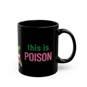 May include: Black ceramic mug with the text "this is POISON" in green and pink. A floral design with pink flowers and green leaves is on the left side of the mug.