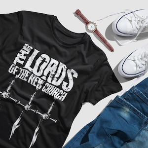 Puede incluir: Una camiseta negra con un estampado gráfico blanco que dice "The Lords of the New Church". El gráfico también incluye tres espadas.