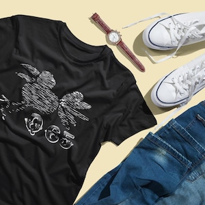 Peut inclure: Un t-shirt noir avec un motif blanc d'oiseau et le texte "OG5". L'image comprend également un jean bleu, des baskets blanches et une montre-bracelet avec un bracelet en cuir marron.