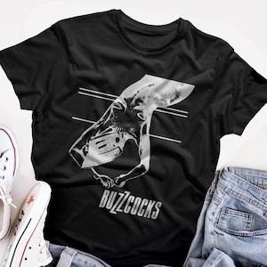 May include: Black t-shirt with a white graphic of a hand holding a cassette tape. The text "Buzzcocks" is printed below the graphic.