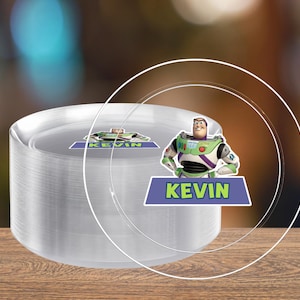 May include: A stack of clear plastic plates with a Buzz Lightyear graphic and the name "KEVIN" on a blue banner. The plates are stacked on a wooden surface.